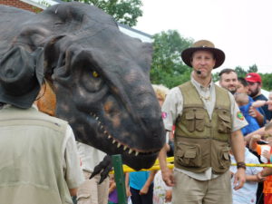 Man facing crowd and educating about fake dinosaur next to him